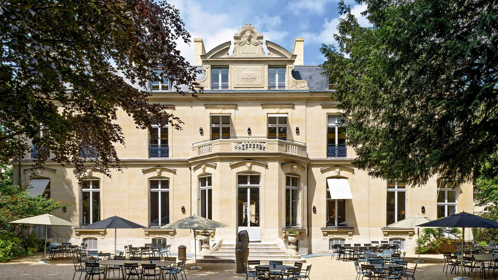 Façade haussmannienne des Salons des Moulures avec terrasse ensoleillée et parasols