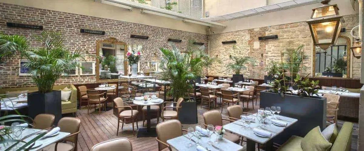 Covered terrace with brick walls, potted palms and dining tables