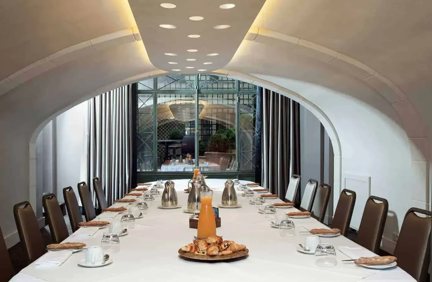 Vaulted salon with a long table set for a meeting and tall windows