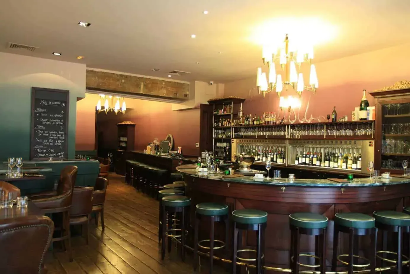 Bar au long comptoir incurvé, tabourets en cuir vert et lustres suspendus